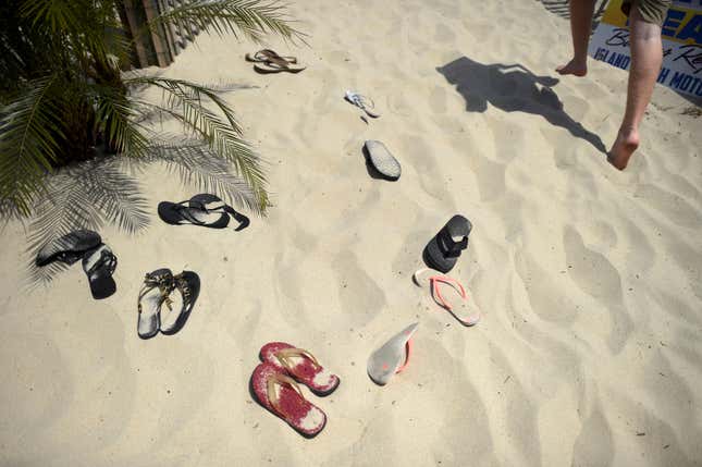 Several pairs of flip-flops sit in the sand. 