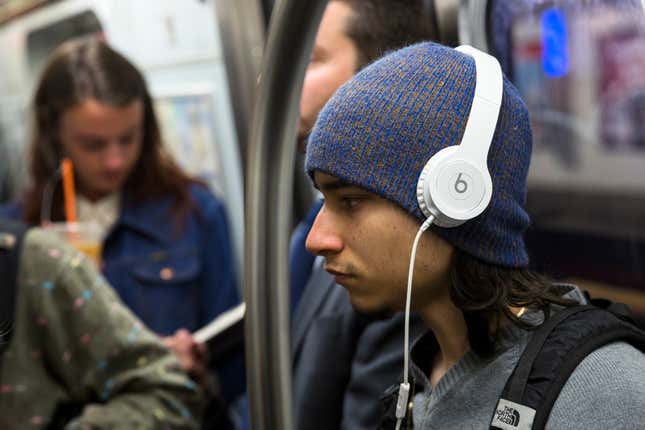A subway commuter in NYC wears a pair of white Beats headphones over their hat. 