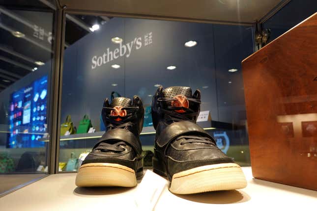 A pair of black Yeezy sneakers with white soles sit in a display case. 